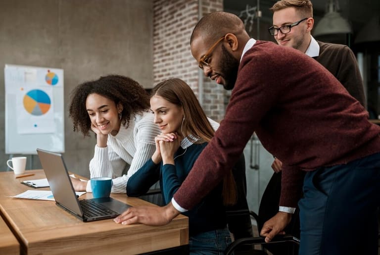 segredos para ser mais feliz no trabalho Grupo de profissionais reunidos em escritório, colaborando e sorrindo durante o trabalho.