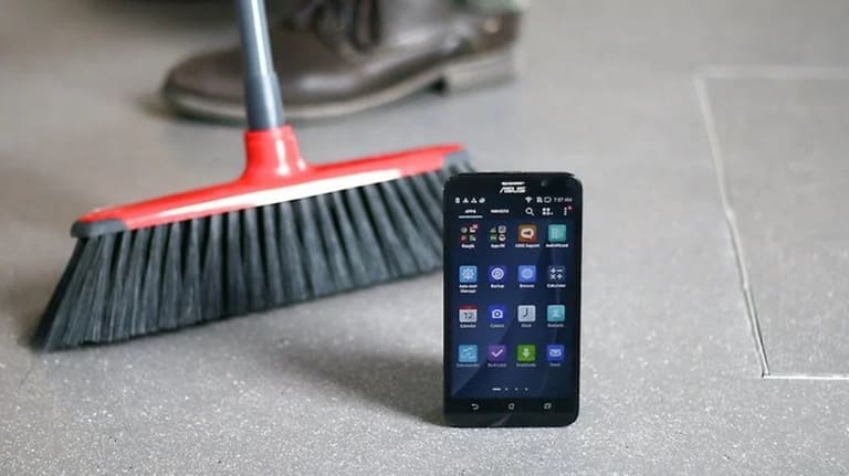 Imagem de um celular ASUS ao lado de uma vassoura, sugerindo a ideia de limpeza digital para celulares.