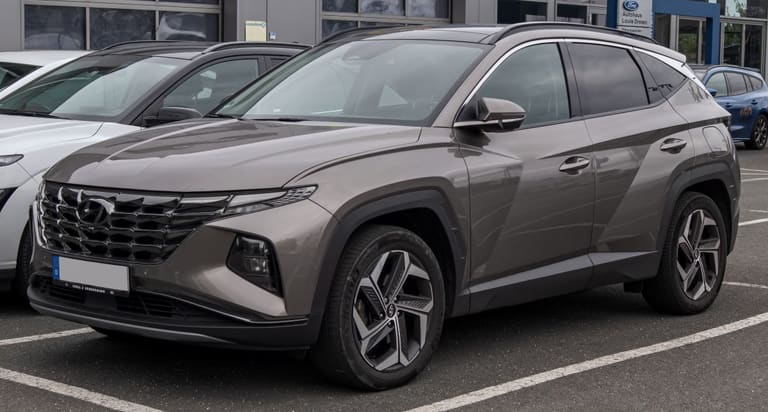 A imagem de um Hyundai Tucson 2024 estacionado em uma rua, visto de frente e de lado.