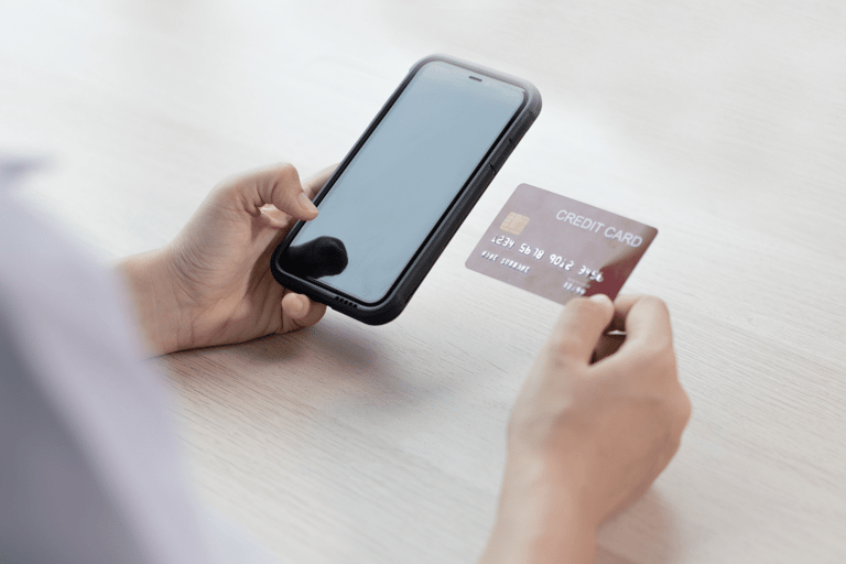 Mãos segurando celular e cartão de crédito para pagamento online na mesa clara