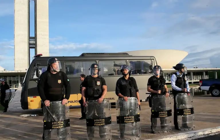 Policiais legislativos federais em frente à Câmara dos Deputados, com escudos e uniforme, preparados para a segurança.