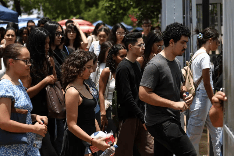 Grupo de jovens segurando garrafas de água, entrando em portão de escola