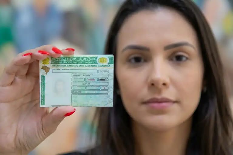 Mulher segurando sua carteira de motorista brasileira, destacando o documento em primeiro plano.