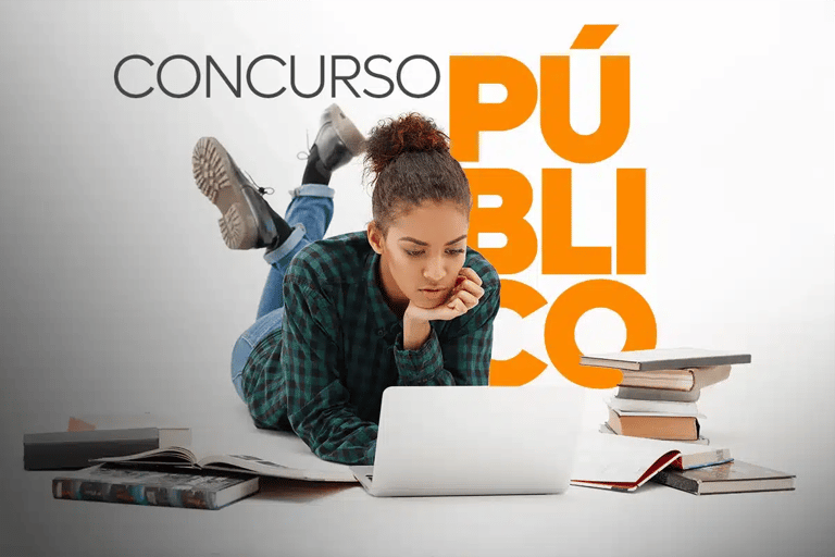 Jovem deitada no chão estudando em notebook ao lado de pilha de livros para concurso público
