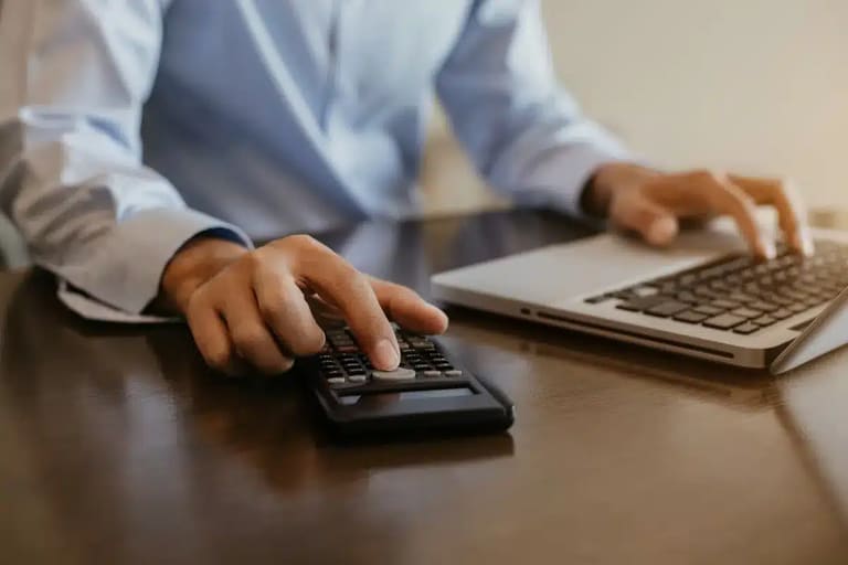 Imposto de Renda 2026 – Declaração de contribuições ao INSS de dependentes Pessoa utilizando calculadora e notebook para organizar valores do Imposto de Renda 2026 e registrar contribuições previdenciárias de dependentes.