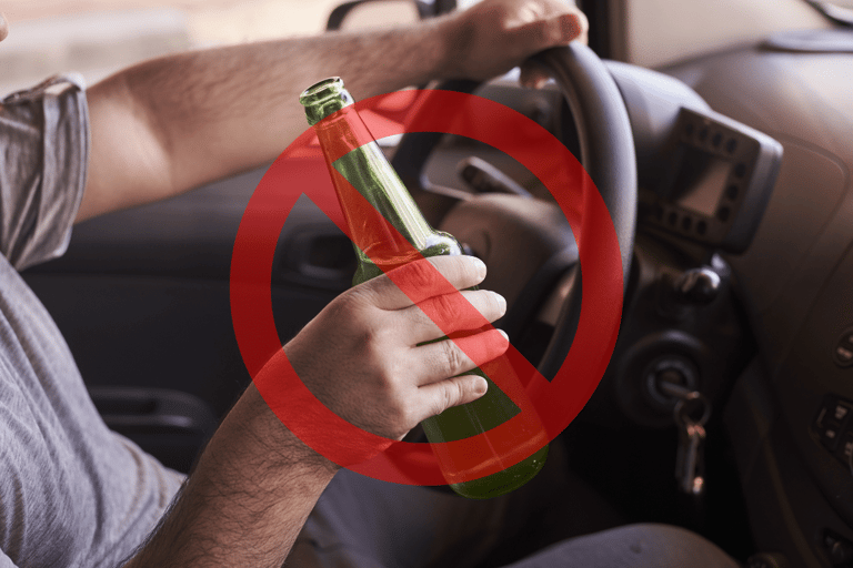 Mão masculina segura garrafa verde de cerveja atrás do volante com sinal vermelho de proibição sobreposto