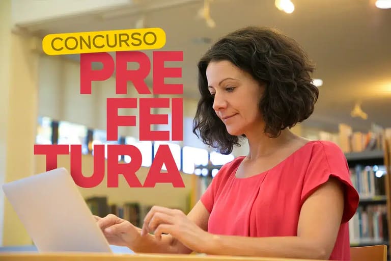 Mulher de blusa rosa sorrindo enquanto digita no notebook em uma biblioteca para se inscrever em concurso