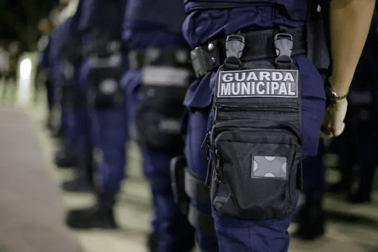 Agentes da Guarda Municipal perfilados em uniforme azul-marinho com brasão e equipamento tático