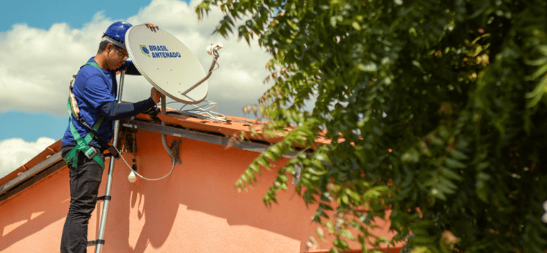 Técnico instala antena parabólica digital Brasil Antenado no telhado de casa residencial