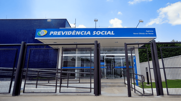 Fachada de uma agência da Previdência Social com grade na entrada e céu azul ao fundo.