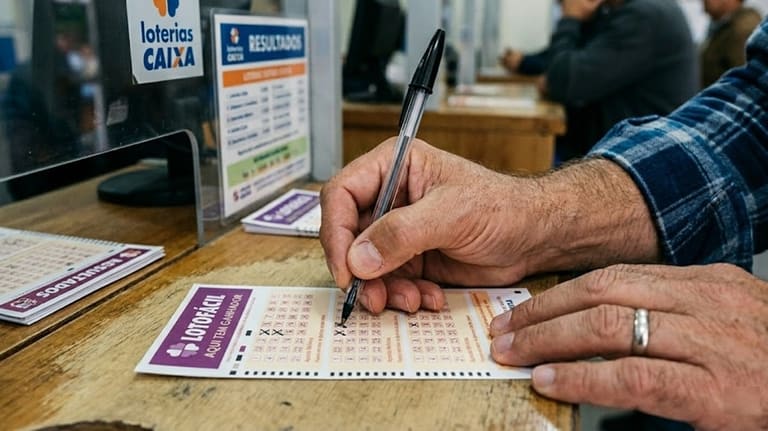 Homem marca volante da Lotofácil com caneta próximo ao balcão de uma lotérica Caixa