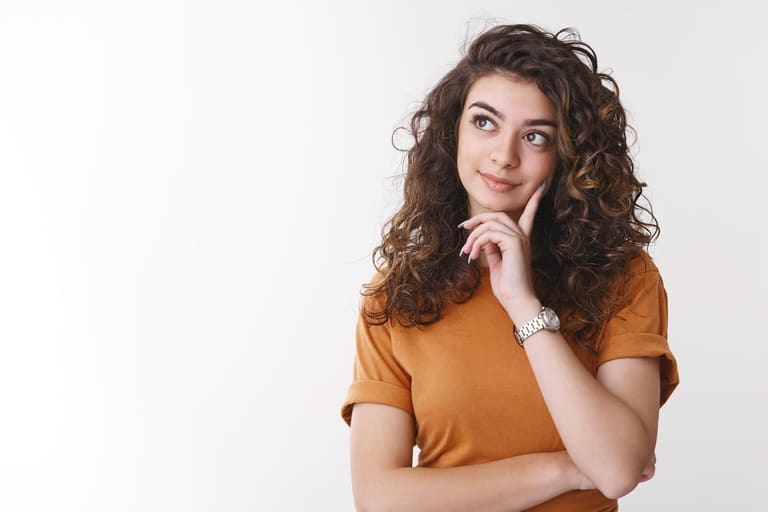 Mulher com expressão pensativa, a mão no rosto, olhando para o lado em fundo claro