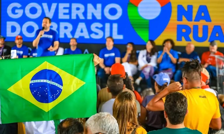 Público acompanha ação do Governo do Brasil na Rua com bandeira do Brasil em destaque durante mutirão de serviços federais.