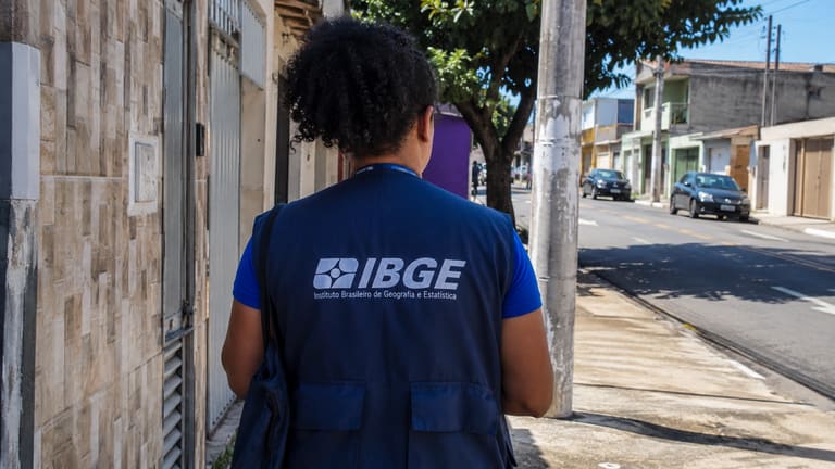 Profissional com uniforme do IBGE em rua residencial durante atividade de campo
