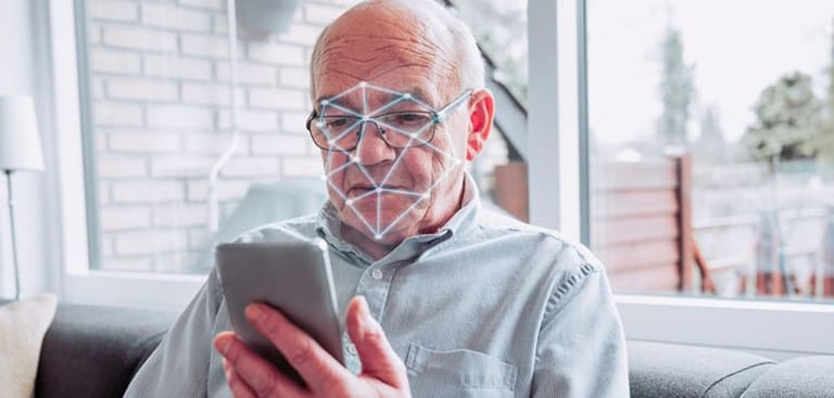 Idoso de óculos realiza reconhecimento facial pelo celular com malha de biometria sobre o rosto
