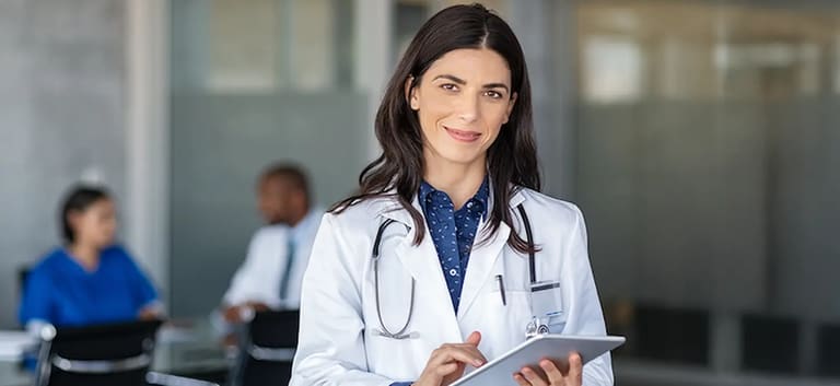 Médica com jaleco e tablet em ambiente hospitalar, representando as inscrições abertas para a primeira etapa do Revalida 2026/2.