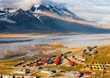 Vista panorâmica de Longyearbyen, Noruega, com casas coloridas, montanhas nevadas e rios congelados ao fundo.