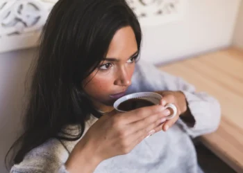 Mulher bebendo café com expressão pensativa, refletindo sobre os efeitos de beber café de estômago vazio.
