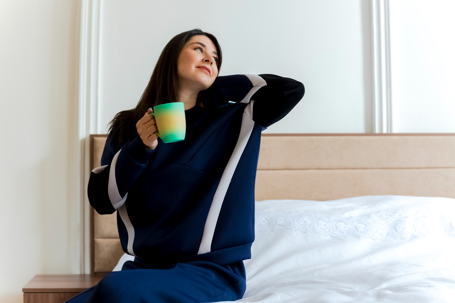 A nova lei trabalhista que pode entrar em vigor e vai mudar seu descanso semanal 2 Mulher relaxada sentada na cama segurando caneca aproveitando momento de descanso em casa.
