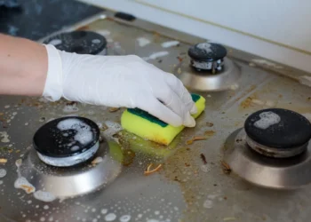 Pessoa limpando gordura do fogão com esponja e luvas