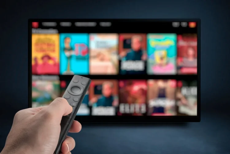 Tela de TV exibindo várias opções de filmes e séries de streaming, com controle remoto em mãos, simbolizando a comparação entre os serviços de Netflix, Max e Prime.