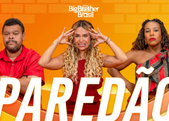 Três participantes em pé, usando roupas vermelhas, com expressões de tensão e expectativa diante do paredão