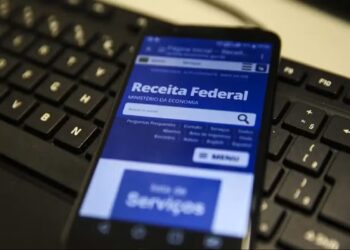 Celular com site da Receita Federal exibido sobre teclado preto de computador