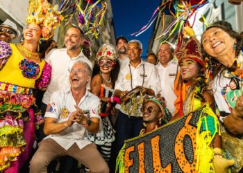Grupo de pessoas fantasiadas sorrindo e celebrando em rua decorada durante o Pré-Carnaval.