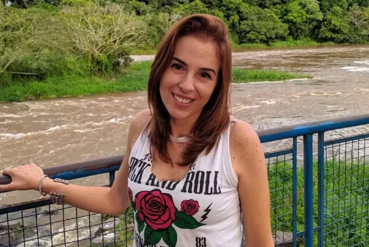 Disputa por herança e furto à casa do tio podem levar Suzane de volta à cadeia; entenda 1 Mulher de cabelos castanhos sorrindo, em ponte azul sobre rio, com camiseta branca, ao ar livre.