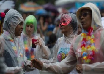 Pessoas fantasiadas usando capas de chuva transparentes festejam durante o Carnaval sob chuva leve
