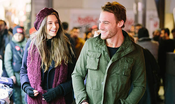 Conheça as novelas turcas mais famosas com Kerem Bürsin, o Serkan de "Será Isso Amor?" 3 Um homem e uma mulher caminham sorridentes em um local público movimentado. A mulher, à esquerda, usa uma boina vinho, cachecol felpudo da mesma cor, casaco escuro e luvas pretas. O homem, à direita, tem cabelos curtos e claros e veste uma jaqueta militar verde sobre uma camiseta preta.