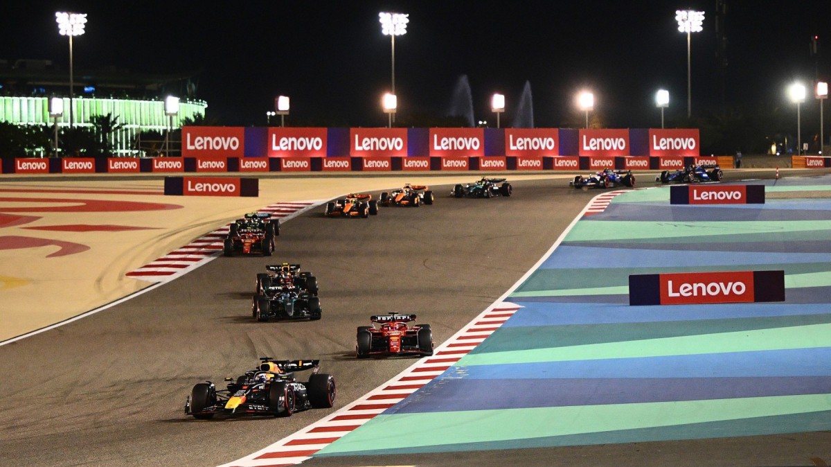 F1 pré-temporada no Bahrein: horários e onde assistir aos testes 2 Diversos carros de Fórmula 1 em fila indiana fazendo uma curva em um circuito iluminado à noite, com destaque para a Red Bull e a Ferrari na frente sob luzes de estádio.
