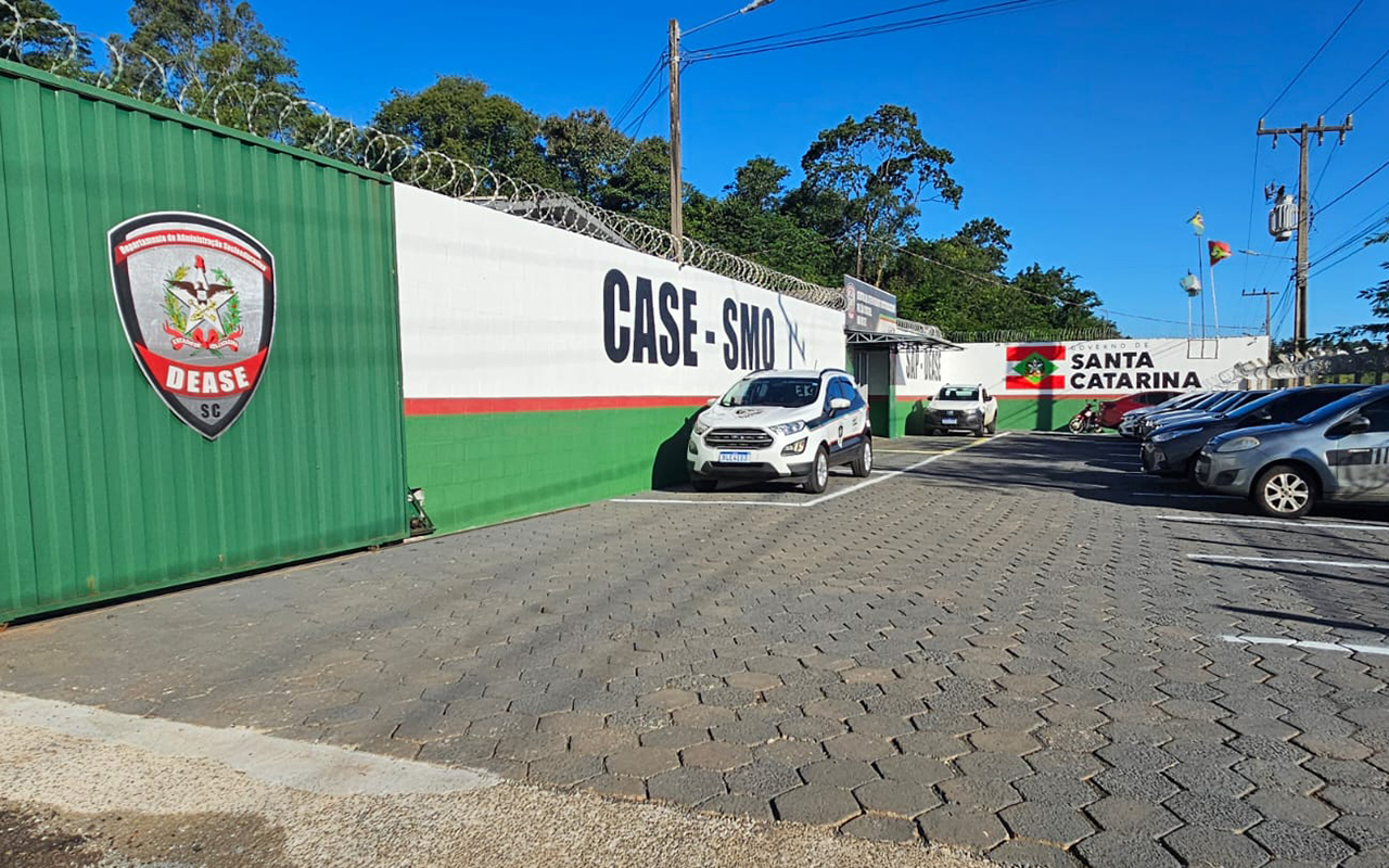 Caso Orelha: onde vai ficar o jovem que matou o cão? Confira como são essas 'prisões' 2 Fachada do CASE SMO em Santa Catarina com muro verde e branco, brasão do DEASE e veículos estacionados.