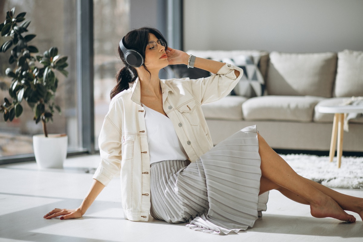 O que as suas "roupas de ficar em casa" dizem sobre você? A ciência revela o impacto silencioso na sua autoestima 2 Mulher relaxando no chão da sala com roupa confortável e estilosa ouvindo música com fones de ouvido