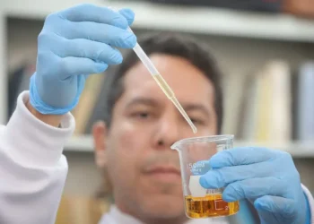 Homem com luvas azuis segurando um béquer com líquido e uma pipeta em laboratório — alerta sobre o aumento de mortes por intoxicação por metanol em São Paulo