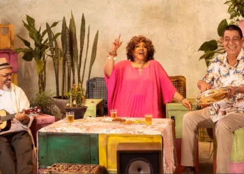 Fãs ganham nova chance: Alcione, Jorge Aragão e Zeca Pagodinho anunciam data extra 8 Grupo musical com instrumentos sentados em mesa rodeada de plantas e bebidas durante show temático.