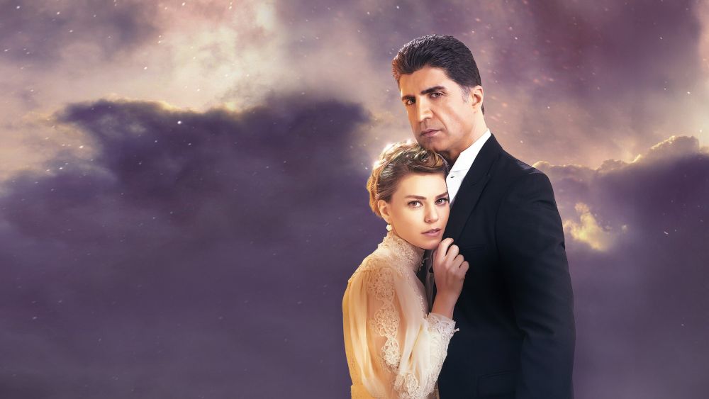 Netflix: 5 séries turcas muito boas que valem a pena assistir 2 Casal protagonista da novela Para Sempre em Meu Coração abraçado. O homem usa terno preto e a mulher um vestido de renda bege. Ao fundo, um céu nublado em tons de roxo e dourado.