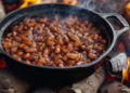 Panela de ferro com feijão cozinhando sobre fogo alto em lenha com chamas ao redor