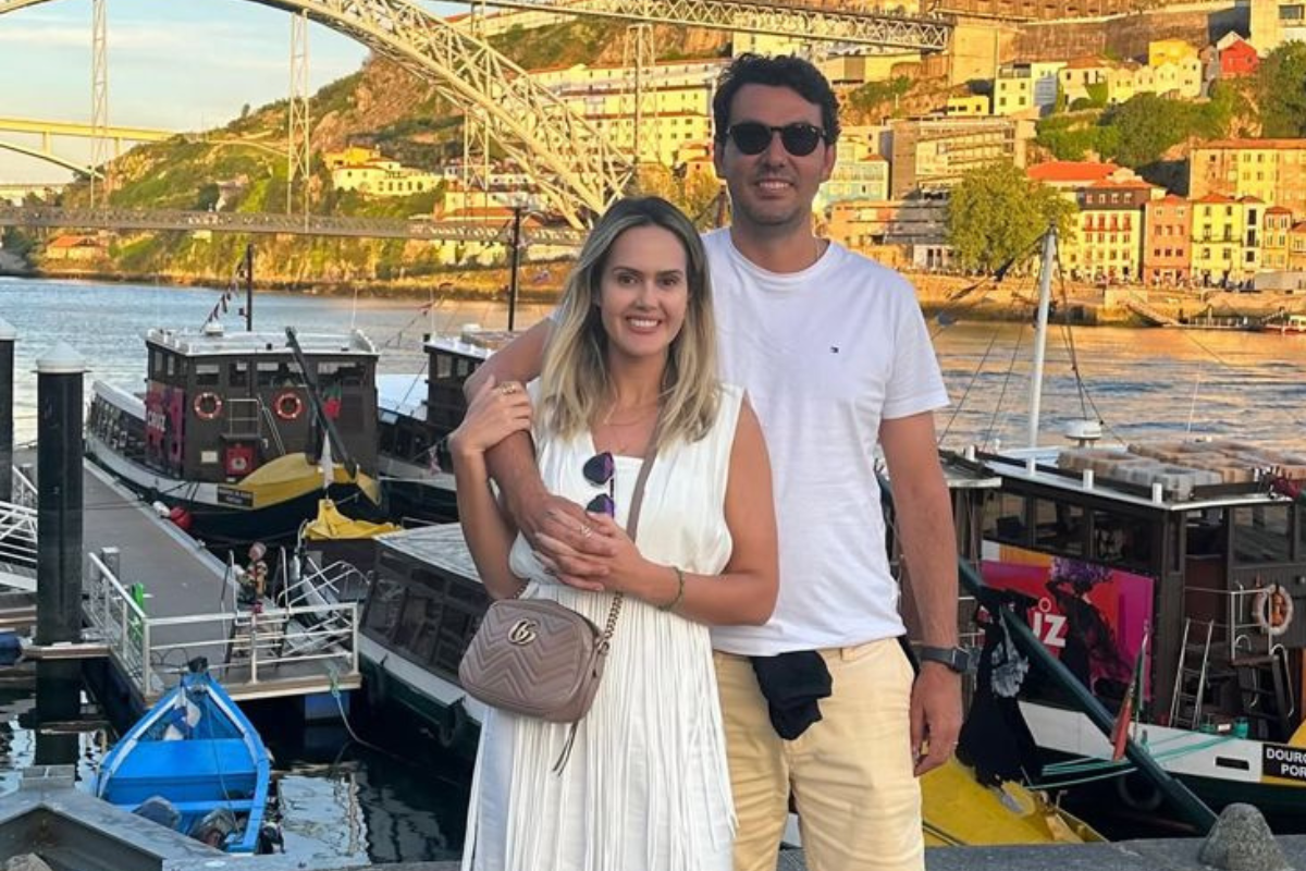 Tragédia familiar em GO: secretário mata filhos e posta carta de despedida antes de tirar a própria vida 3 Casal sorridente posa de frente para barcos atracados no cais com ponte ao fundo