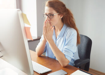 Portrait of young female writer thinking on text for a new book via PC while sitting in co-working space, pretty student girl busy working on course-work with concentrated expression.