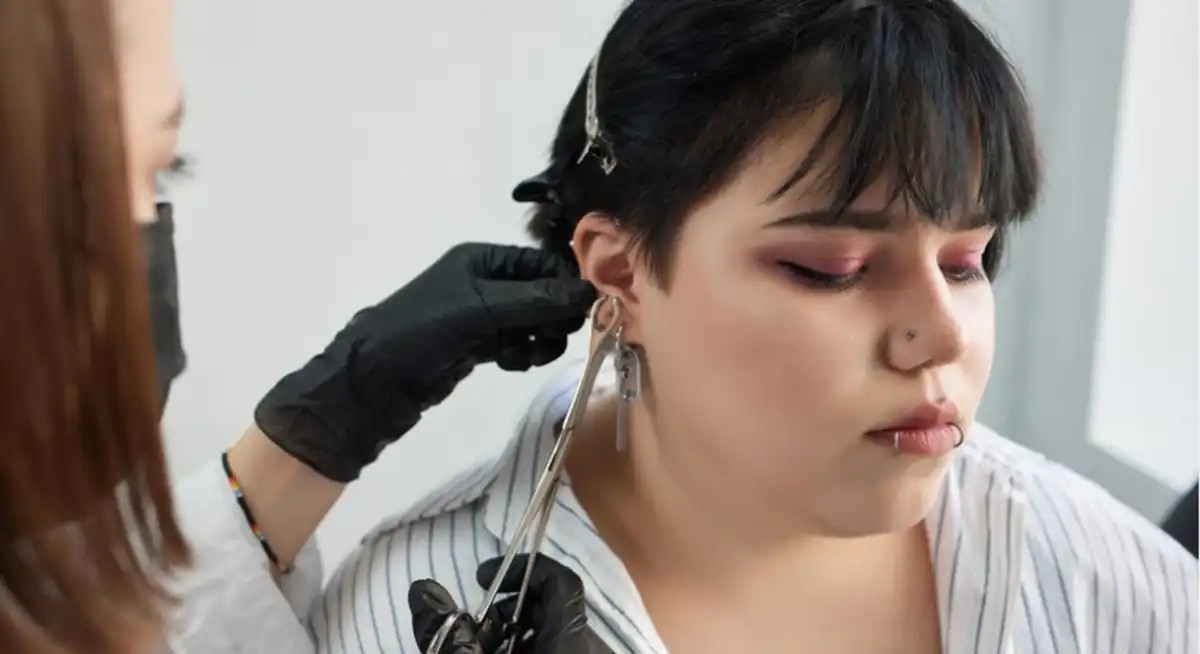 uso da salmoura cicatrização piercing Profissional realizando o furo de um piercing em orelha de uma cliente, representando o processo de cicatrização.