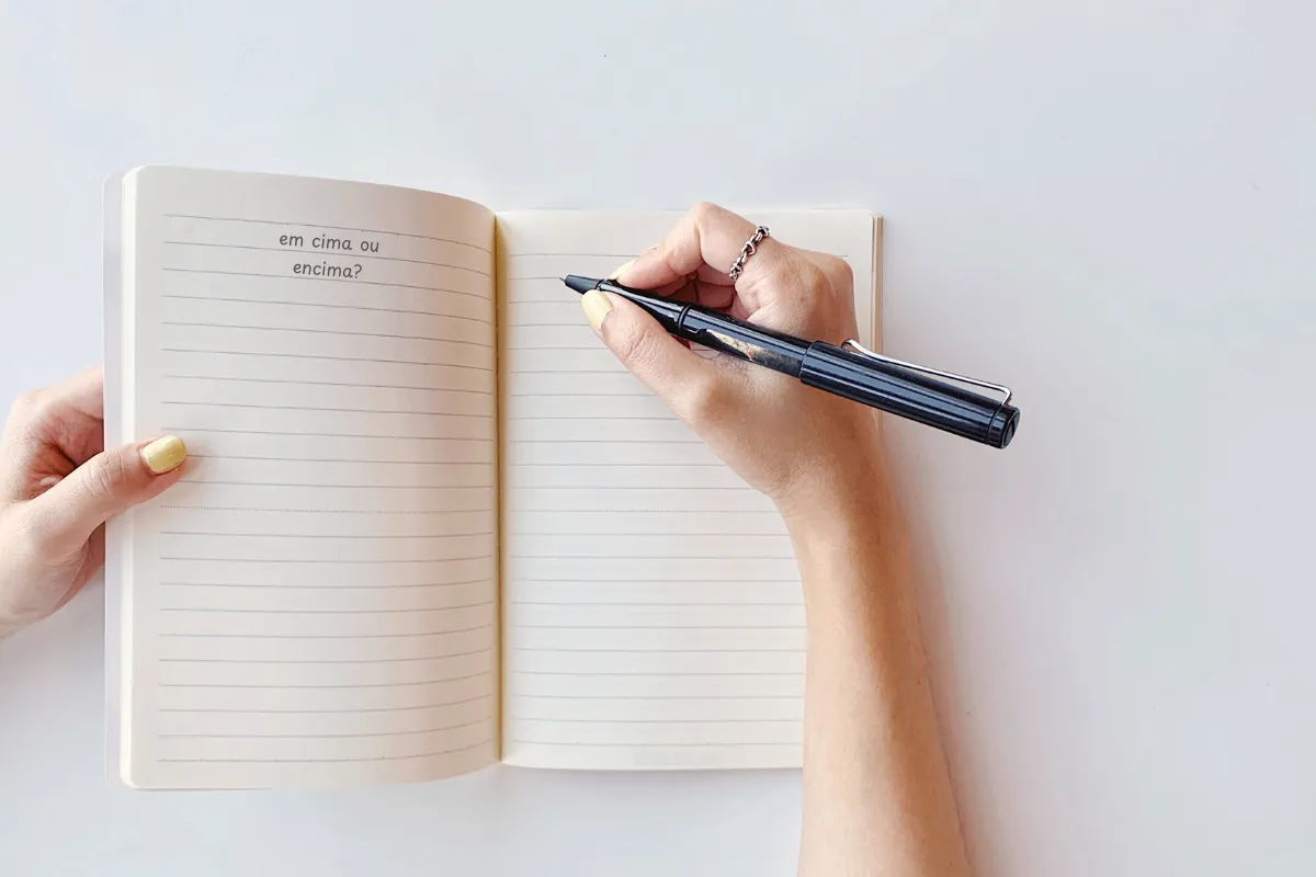 Diferença entre em cima e encima – dúvida comum no português Pessoa escrevendo em caderno com a dúvida: em cima ou encima?