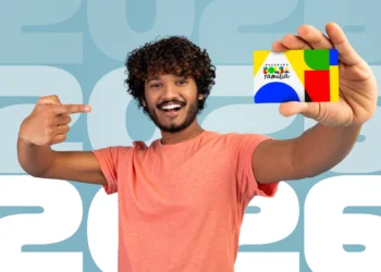 Homem sorridente segurando e apontando para o cartão do programa Bolsa Família em frente a um fundo com o ano 2026.