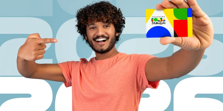 Homem sorridente segurando e apontando para o cartão do programa Bolsa Família em frente a um fundo com o ano 2026.