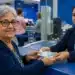 Idosa recebendo dinheiro de uma atendente em agência bancária, representando o pagamento de benefícios do INSS em julho de 2026.