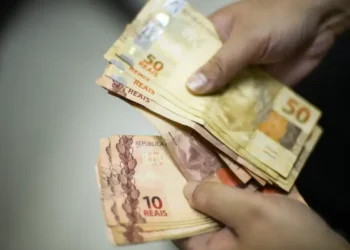 Pessoa contando cédulas de 50 e 10 reais, em uma possível transação de dinheiro.