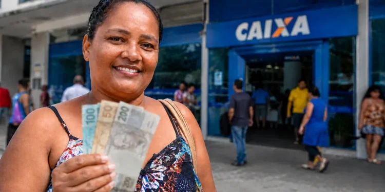 Mulher segura notas de reais em frente a uma agência da Caixa, representando o pagamento do Bolsa Família nesta sexta-feira (21 de agosto).