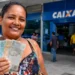 Mulher segura notas de reais em frente a uma agência da Caixa, representando o pagamento do Bolsa Família nesta sexta-feira (21 de agosto).