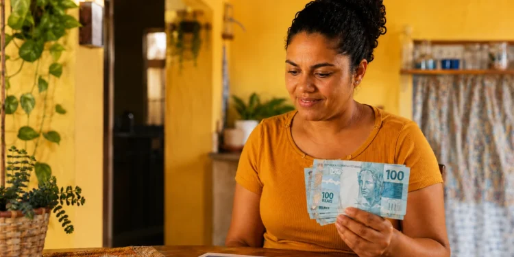 Mulher segura notas de R$ 100 ao lado de calendário de setembro, em referência às datas de pagamento do Bolsa Família.