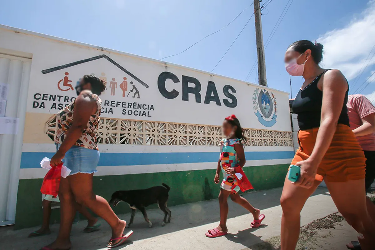 CRAS - Centro de Referência da Assistência Social Pessoas caminhando em frente ao Centro de Referência da Assistência Social (CRAS), com uma criança e um cachorro visíveis.